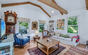 A spacious living room with a large wooden ceiling, a classic clock, a blue armchair, a wooden coffee table, and a white sofa. - Woodstock Vermont Escape with Space to Slow Down (Woodstock)