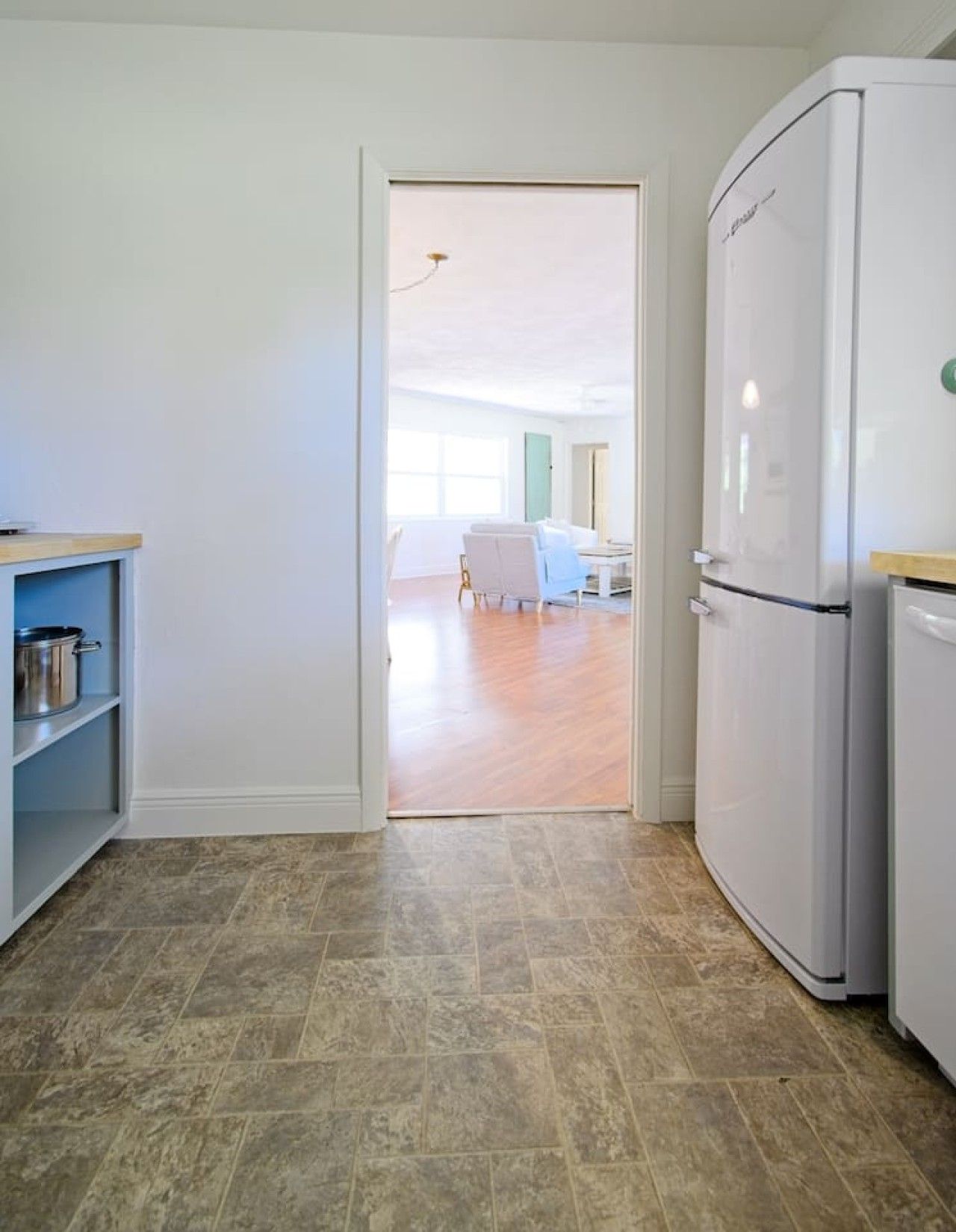 A kitchen with a white refrigerator, a wooden countertop, and a tiled floor.