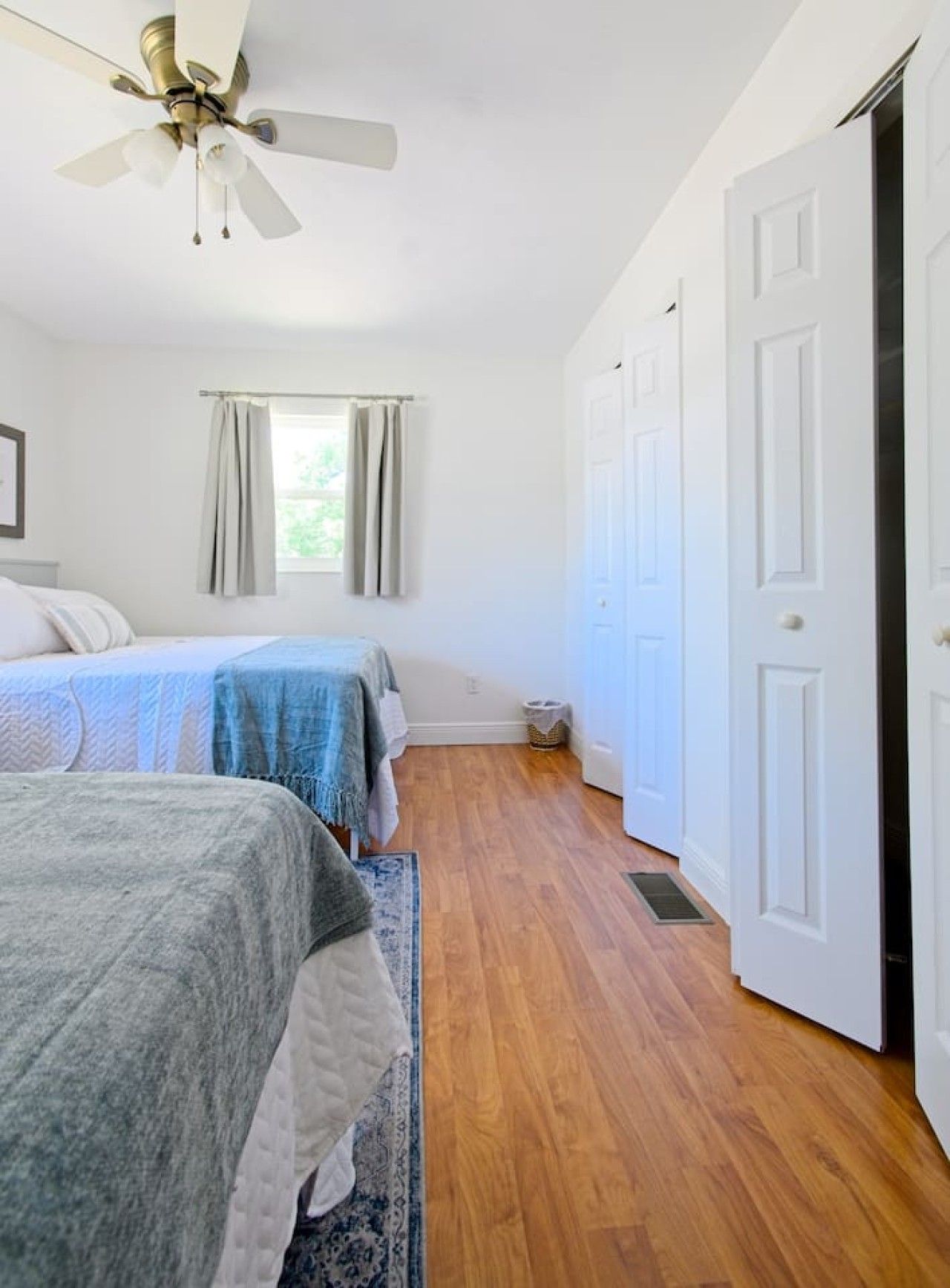 Une chambre avec deux lits, un ventilateur de plafond, une fenêtre avec des rideaux et une porte.
