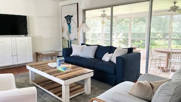 A modern living room with a dark blue sofa, a wooden coffee table, and a large window providing a view of the outdoors.