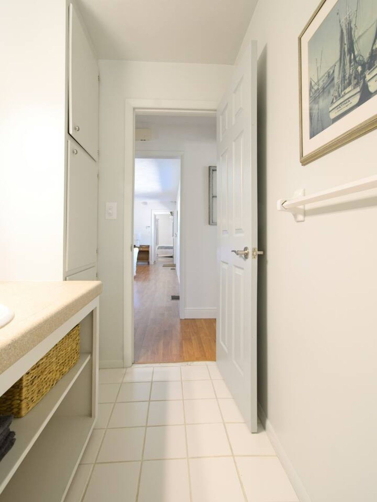 A narrow hallway with a white door leading to a room with a wooden floor.