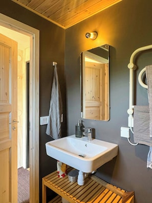 A bathroom with a wooden door, a white sink, a mirror, and a towel rack. - Renovated house with garden in Österlen (Skåne län)