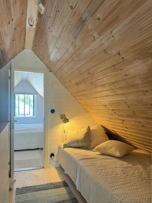 A bedroom with a sloped ceiling, a bed with pillows, a bedside lamp, and a window. - Renovated house with garden in Österlen (Skåne län)