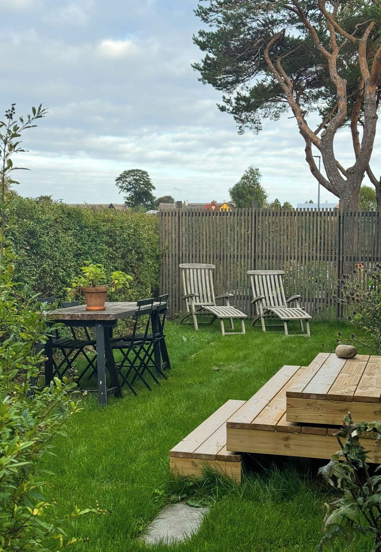 A backyard with a wooden table and chairs, a potted plant, and a wooden deck.