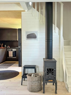A modern kitchen with a built-in wood stove, a wicker basket, and a black stool.