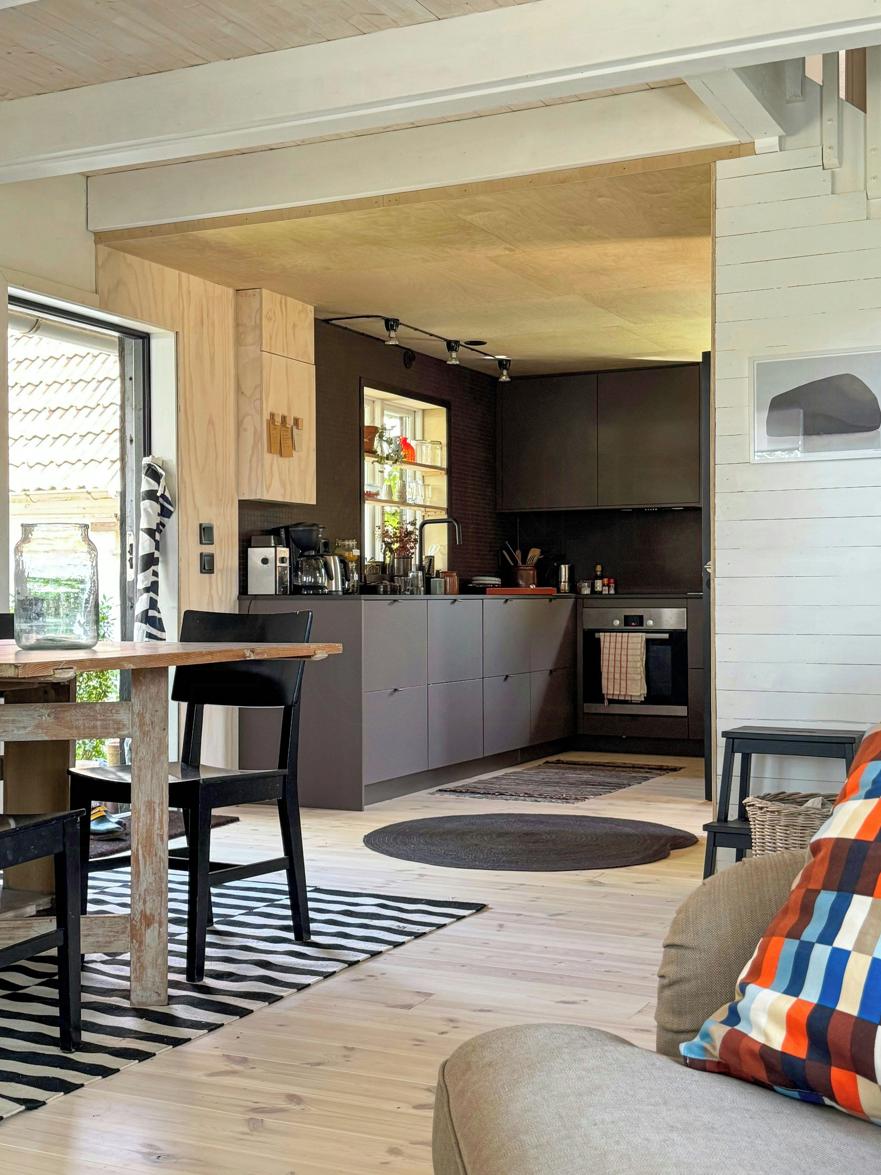 Une cuisine moderne avec des meubles gris, un îlot central et un coin repas comprenant une table en bois et des chaises noires.