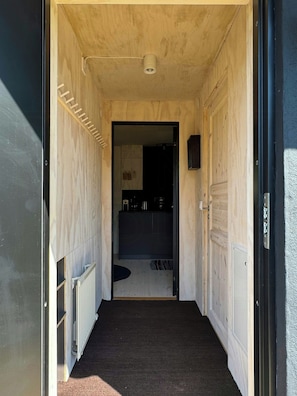 A narrow hallway with a radiator on the left, a dark carpet, and a door leading to a room with a dark interior.