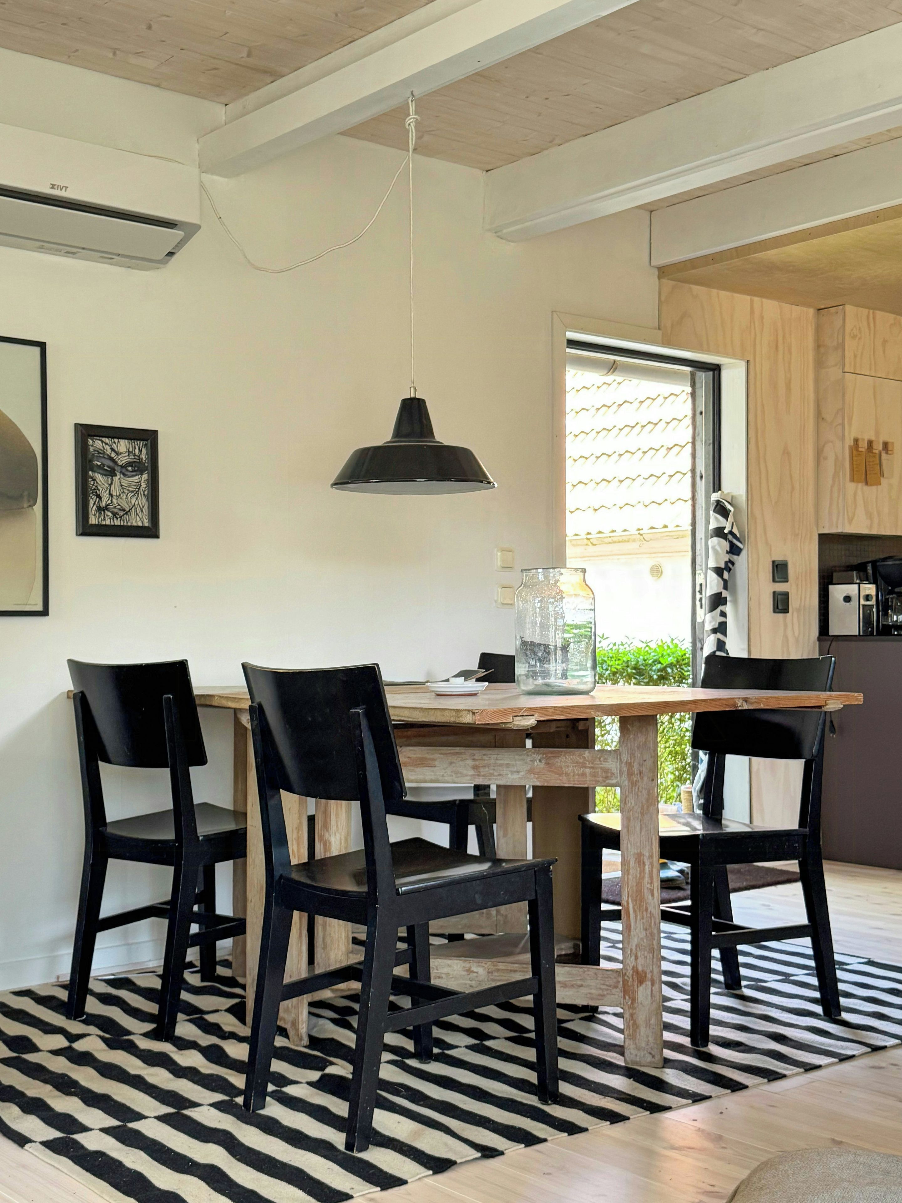 Une cuisine moderne avec une table en bois, des chaises noires et un luminaire suspendu.