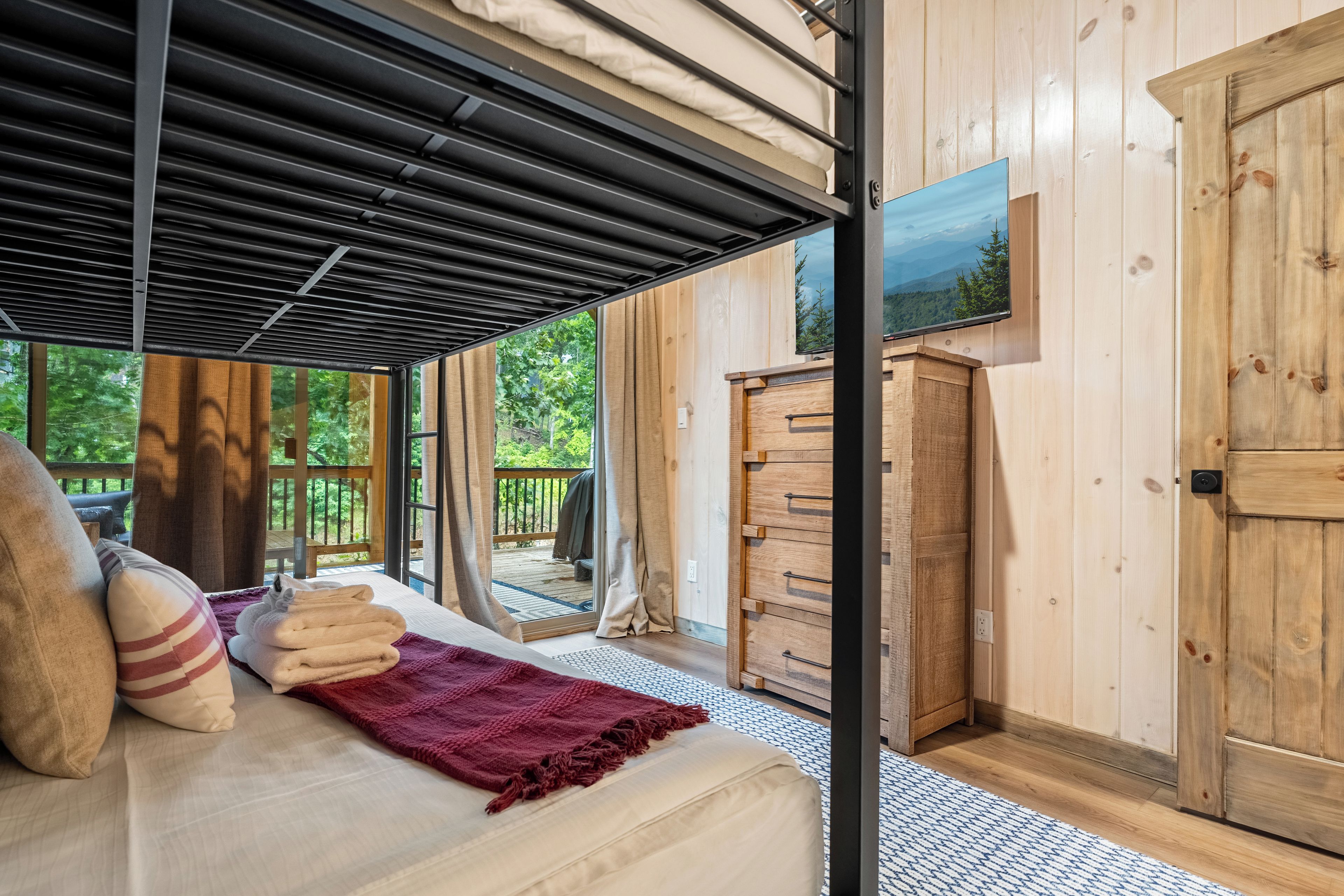 A bedroom with a bed, a window, a wooden wardrobe, and a view of the outdoors.