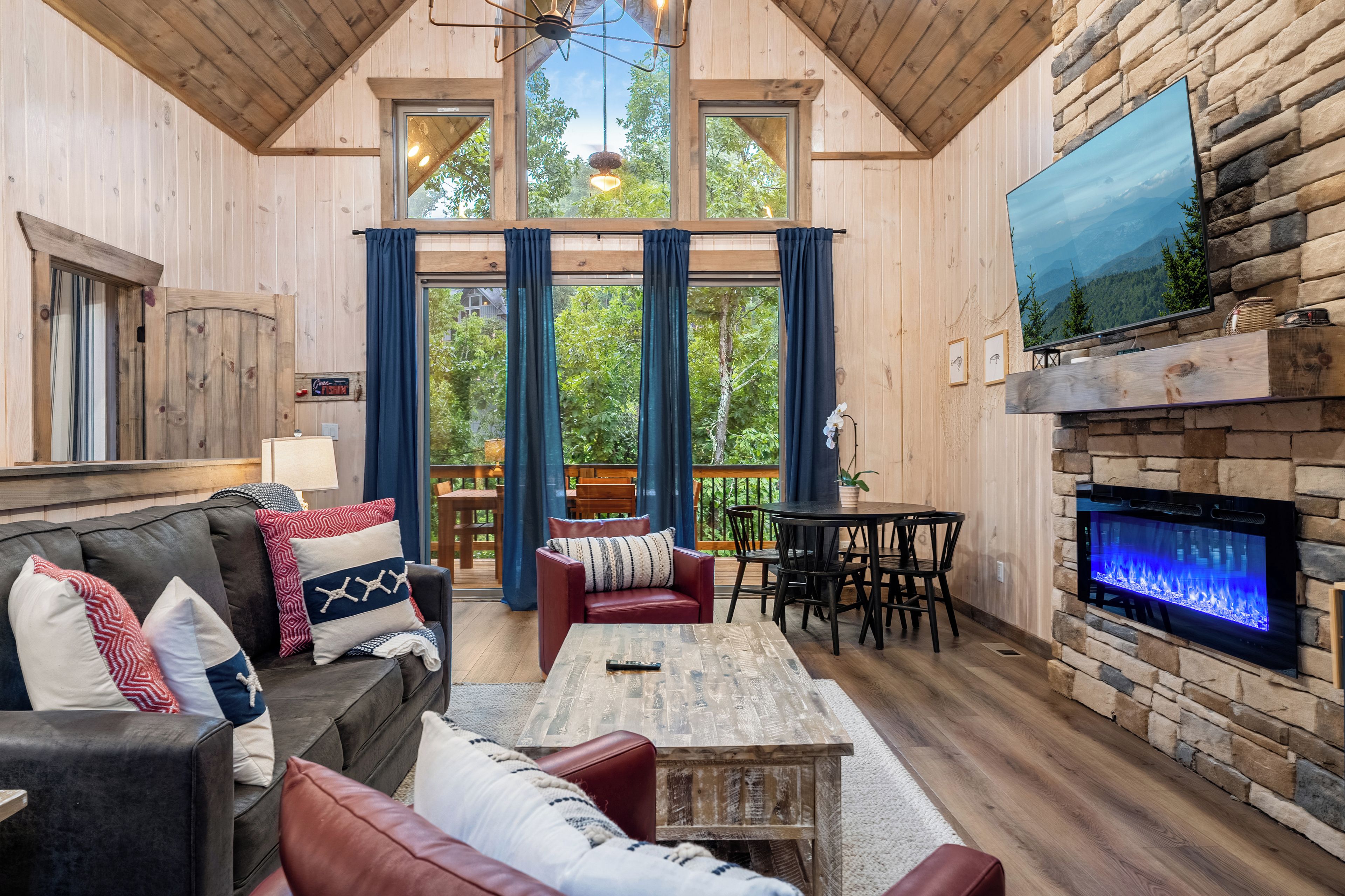 Un salon chaleureux avec une cheminée, des murs en bois et une grande fenêtre donnant sur un paysage verdoyant.