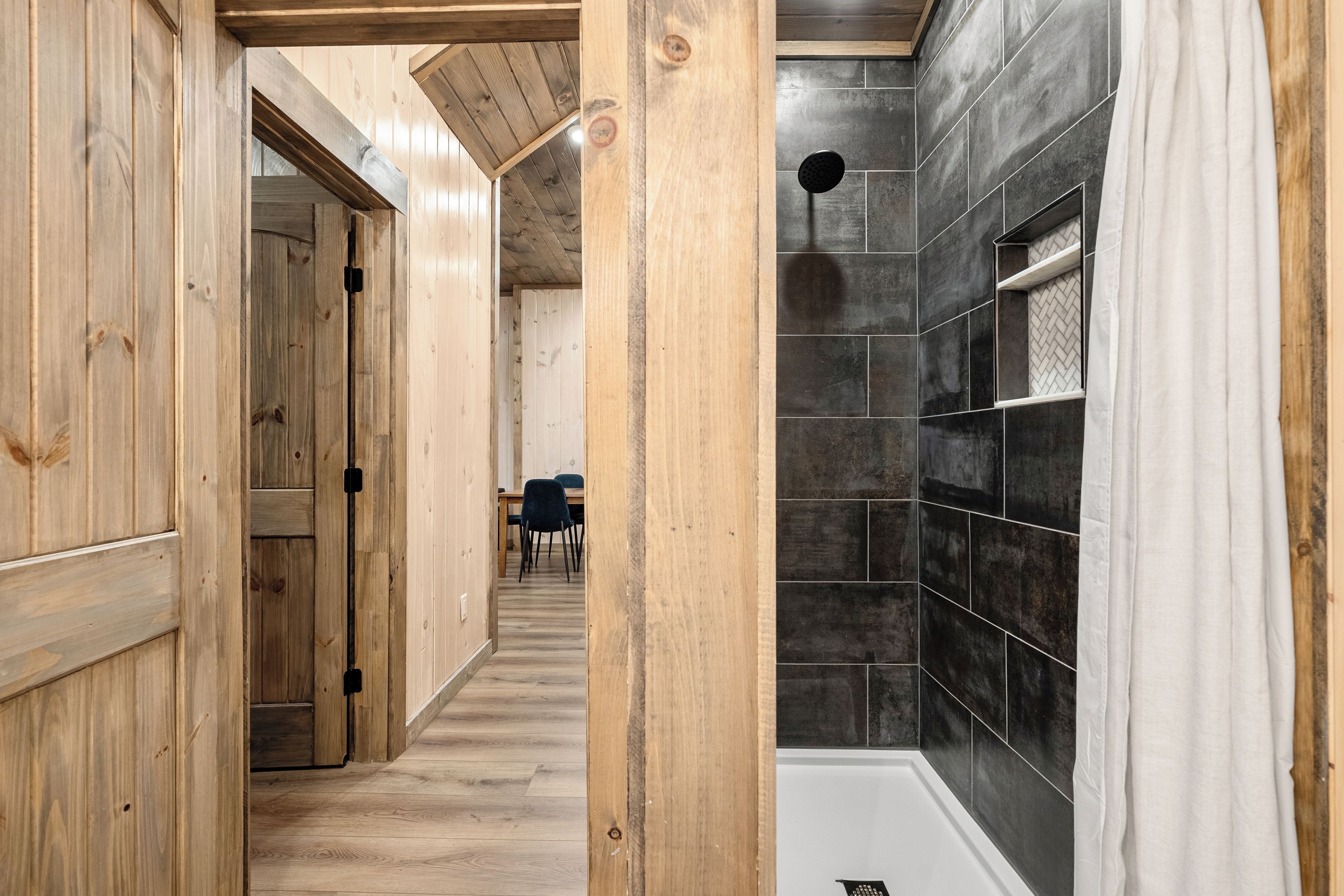 A wooden interior hallway leading to a bathroom with a shower and tiled walls.