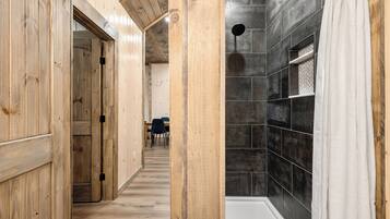 A wooden interior hallway leading to a bathroom with a shower and tiled walls.
