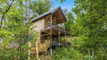 A multi-level wooden cabin with a balcony, surrounded by dense forest.
