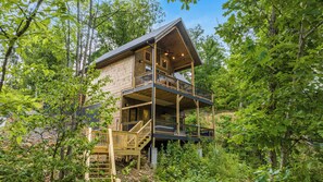 A multi-level wooden cabin with a balcony, surrounded by dense forest. - Lakefront-Private Dock-Pets-Hot Tub-Beach Access (Sevierville)