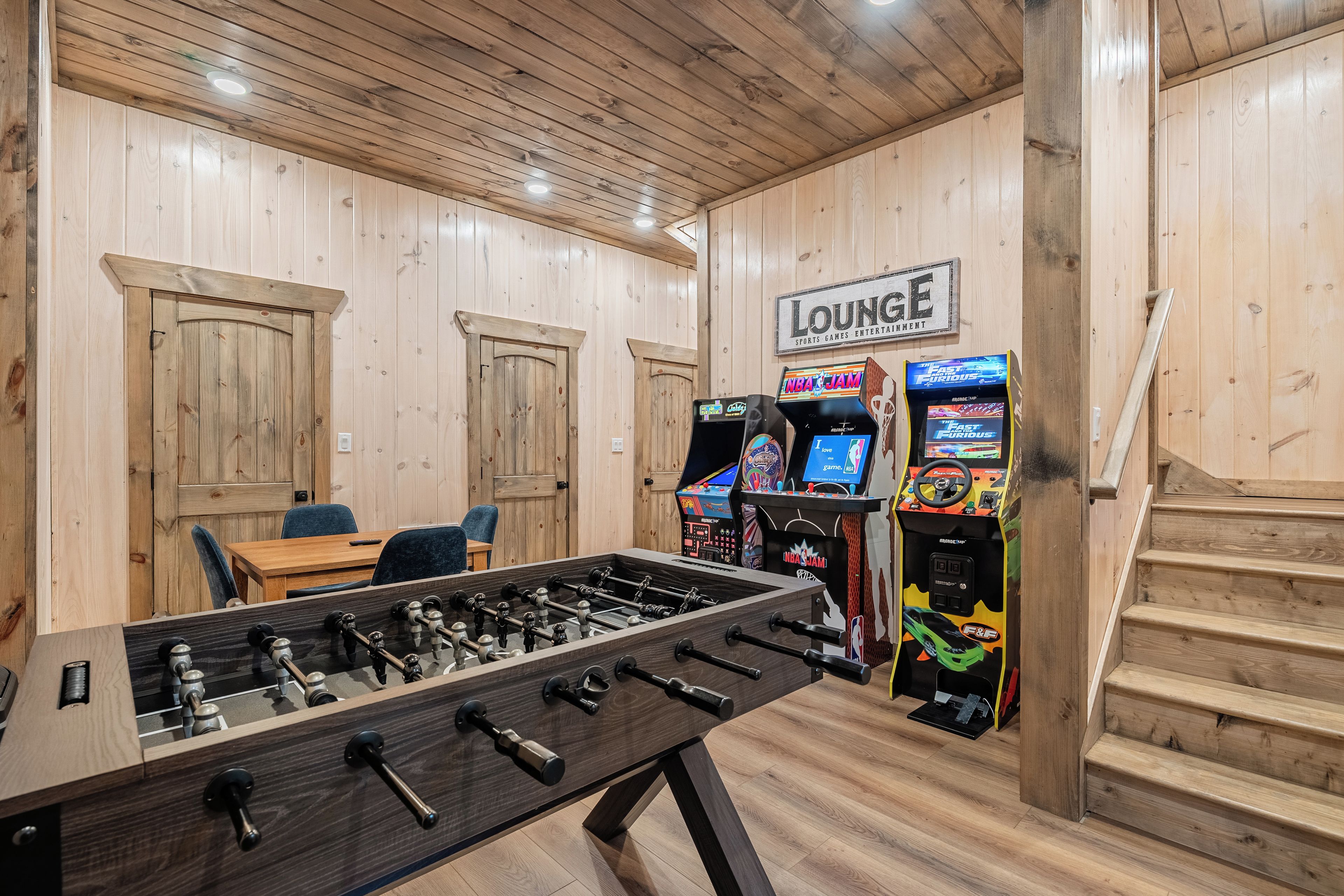 A room with a foosball table, two doors, a lounge area, and arcade games.