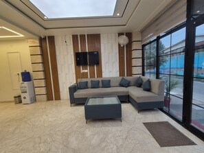 A modern interior with a sectional sofa, a glass coffee table, a flat-screen TV mounted on the wall, and a water dispenser.