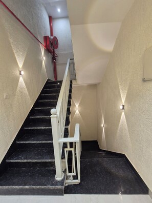 A staircase with black steps and white railings, leading to a landing with a red pipe and a white chair.