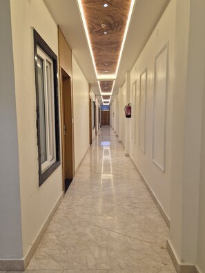 Un pasillo largo y estrecho con piso de mármol pulido, puertas de madera e iluminación empotrada en el techo.