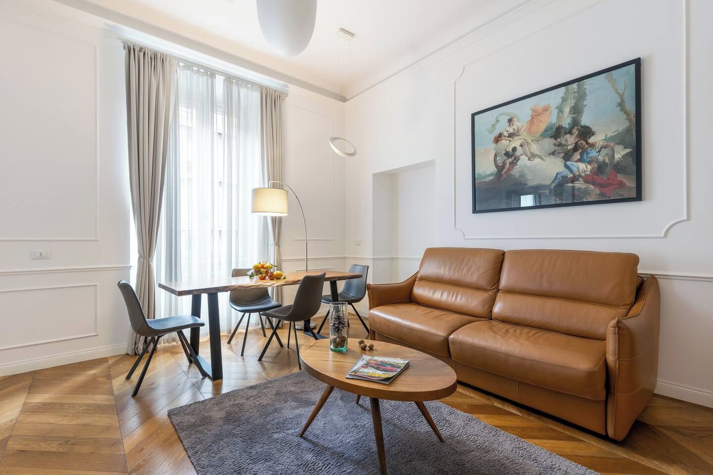 Ein modernes Wohnzimmer mit einer braunen Ledersofa, einem Esstisch mit Stühlen, einem Couchtisch und einem Gemälde an der Wand.