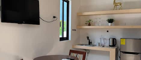 A compact kitchen with a built-in TV, a dining area with two chairs, a window, and a stainless steel refrigerator.