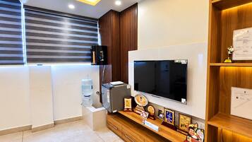 A modern office space with a flat-screen TV mounted on the wall, a water dispenser, a small refrigerator, and a wooden cabinet with awards.