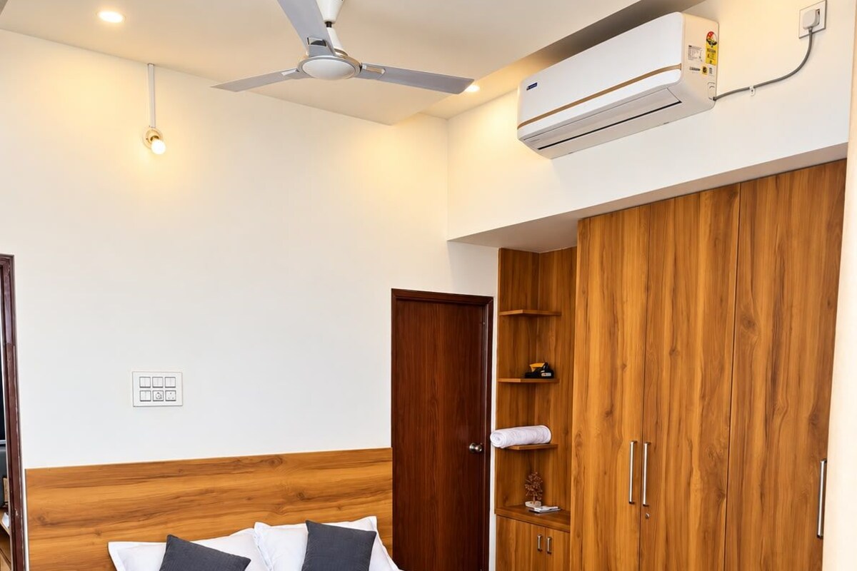 A bedroom with a bed, wooden wardrobe, ceiling fan, and air conditioning unit.