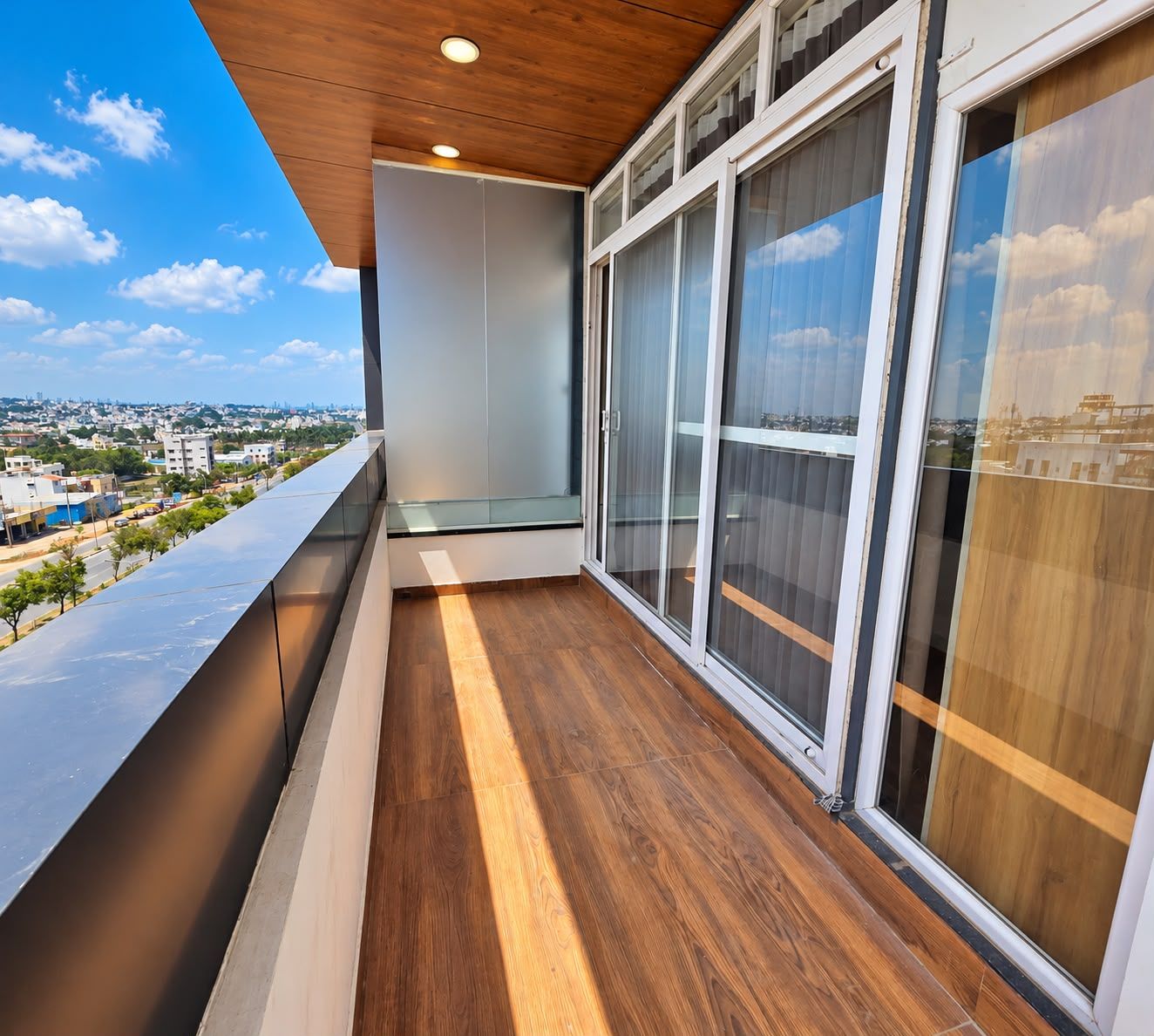 A balcony with a wooden floor and large windows overlooking a cityscape.