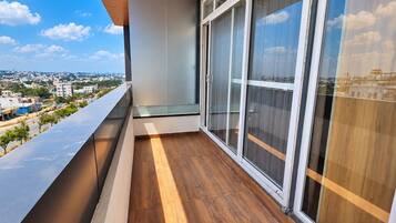 A balcony with a wooden floor and large windows overlooking a cityscape.