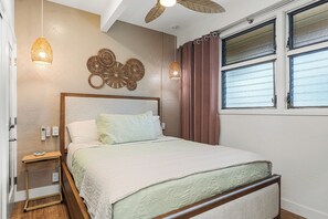 Ein Schlafzimmer mit Bett, Nachttisch, Wandleuchten und einem Fenster mit Vorhängen.