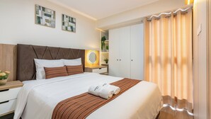 Ein ordentlich gemachtes Bett mit einer gestreiften Decke und Kissen, ein Nachttisch mit Lampe, ein Spiegel und ein an der Wand befestigtes Regal mit Pflanzen.