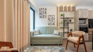 Ein modernes Wohnzimmer mit einer Couch, einem Holzstuhl, einem Teppich und einer Küchenzeile mit Geräten.