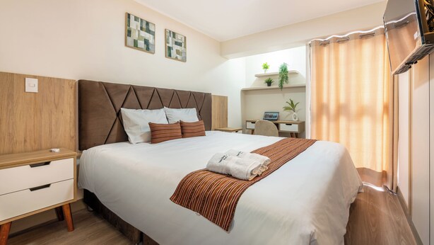 Ein Hotelzimmer mit einem Bett, einem Nachttisch, einem Schreibtisch, einem Stuhl und einer kleinen Pflanze auf einem Regal.