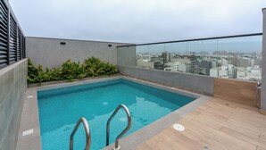 Ein Pool auf dem Dach mit Blick auf die Stadt, umgeben von Grünflächen und moderner Architektur.