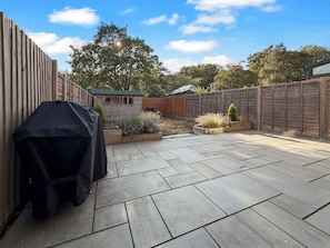 A patio area with a barbecue grill, a wooden fence, and a small shed.