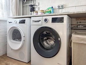 Two front-loading washing machines in a laundry area with a white brick wall and a window with curtains.