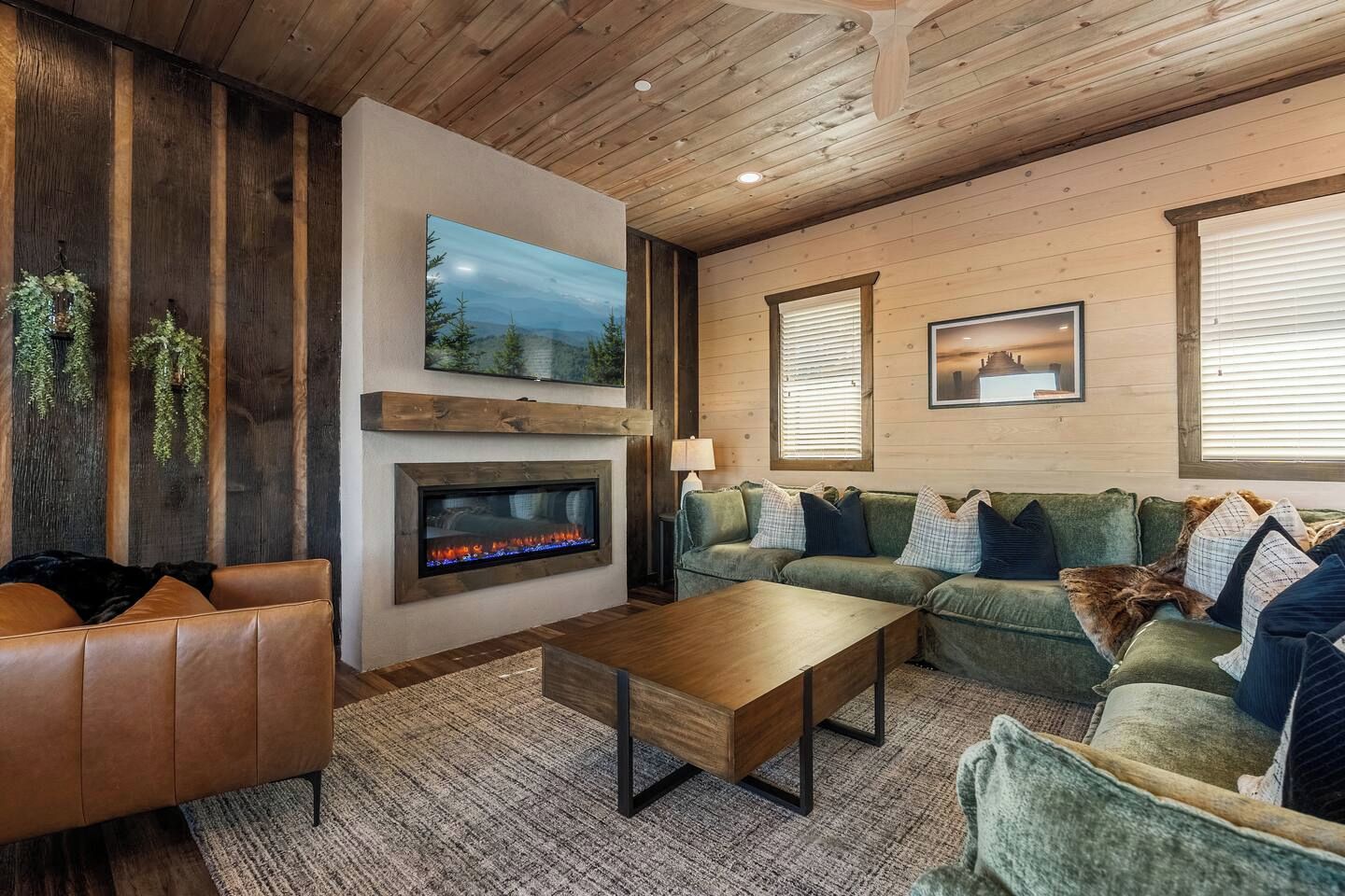 A cozy living room with a fireplace, a green sofa, a brown leather couch, and a wooden coffee table.