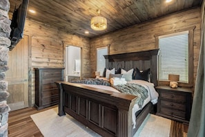 Un dormitorio con cabecera de madera, una cama grande, un aparador y una pared de piedra.