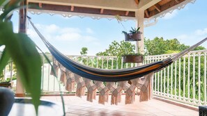 A hammock on a balcony with a white railing, potted plants, and a clear sky. - Villa Ladouchka 3 étoiles, loft créole jusqu'à 7 pers. Entre randos et plages. (Goyave)