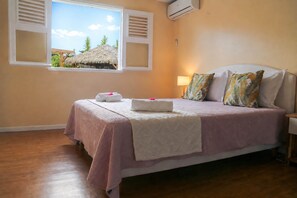 Un dormitorio con cama, almohadas, mesita de noche, lámpara y aire acondicionado.