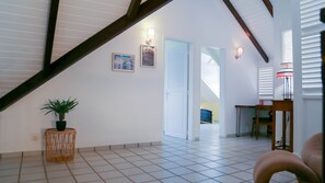 Un pasillo amplio con piso de baldosas, una escalera con vigas de madera y una puerta que da a otra habitación.