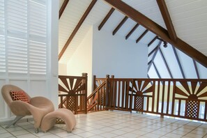 Una habitación amplia con techo alto, una escalera de madera y un sillón acolchado.