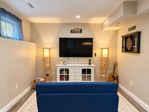 Una sala de estar con un televisor de pantalla plana, un dardo, una guitarra y un sofá azul.