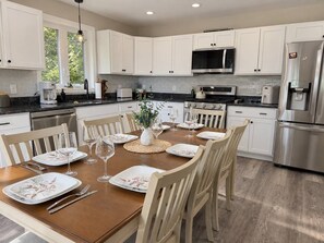 Cocina moderna con armarios blancos, electrodomésticos de acero inoxidable y una mesa de comedor dispuesta para seis personas.