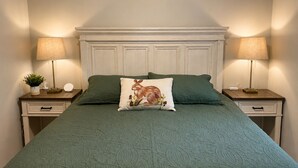 Ein Bett mit einer grünen Tagesdecke, zwei Nachttische mit Lampen und ein dekoratives Kissen.