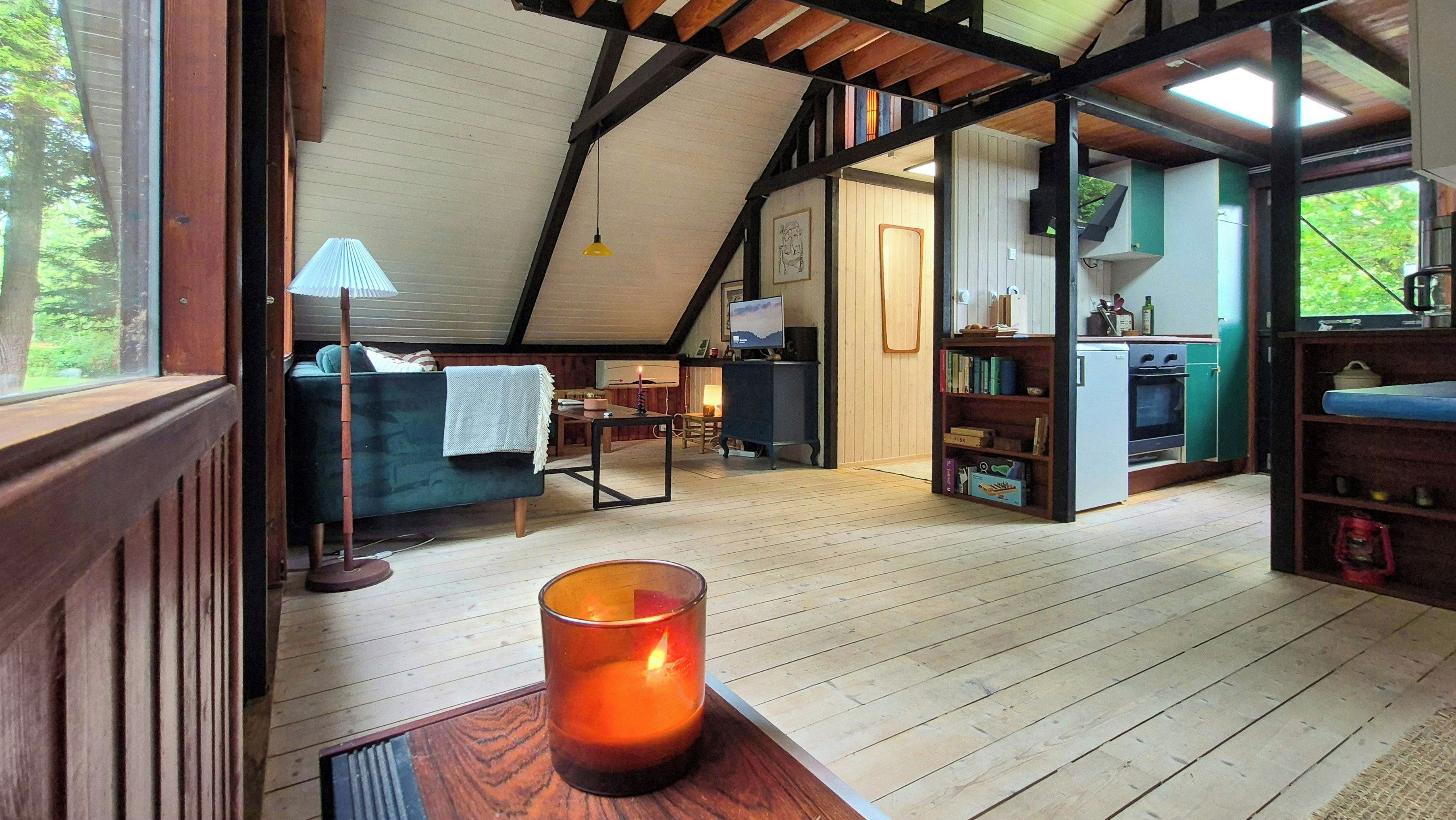 A cozy attic room with a wooden floor, a sofa, a table with a candle, and a television.