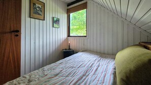 Una habitación con una cama, una ventana, una puerta y una pequeña mesa con una vela.