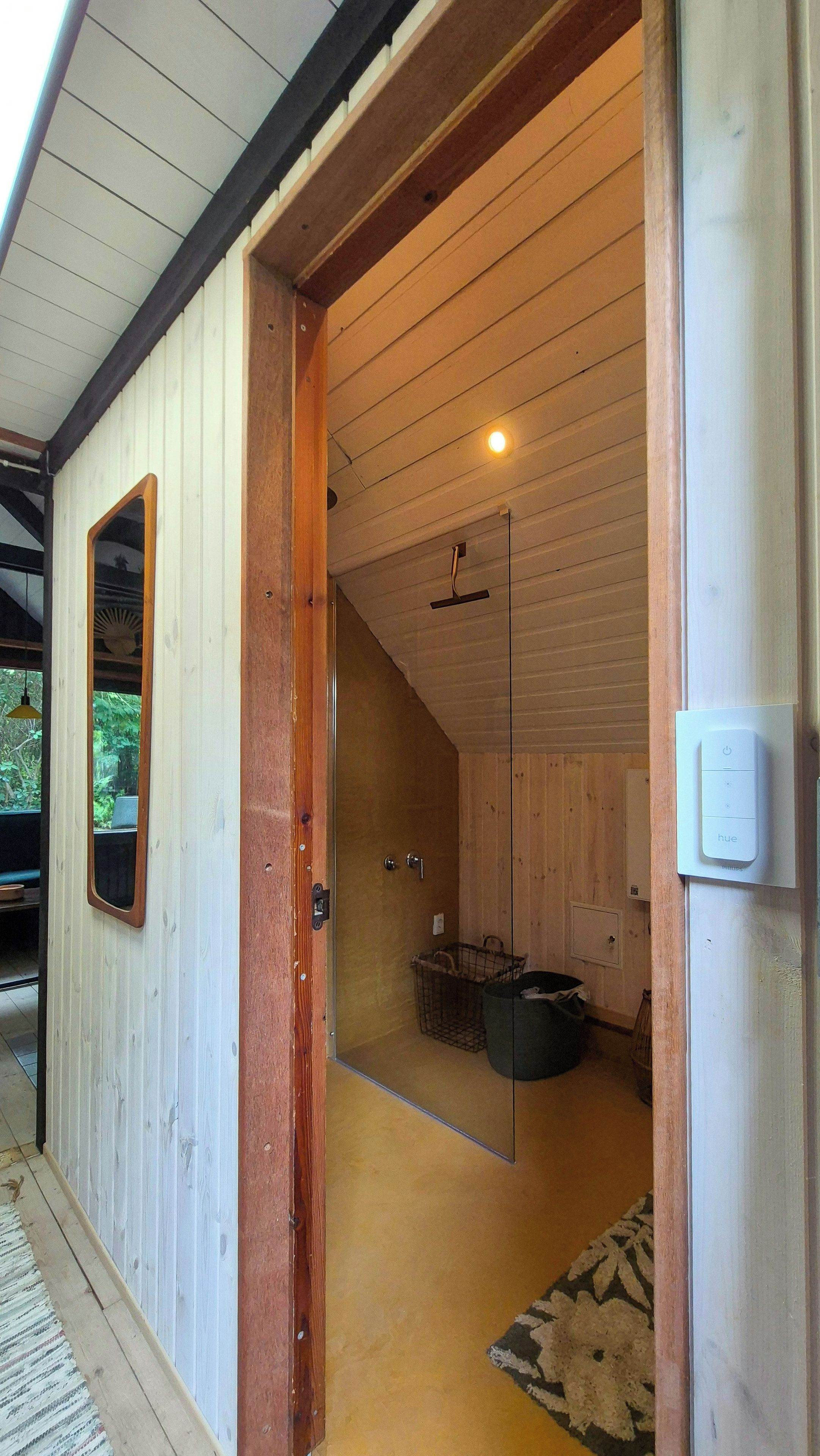 A wooden interior with a glass door leading to a bathroom, a hanging light fixture, and a visible power outlet.