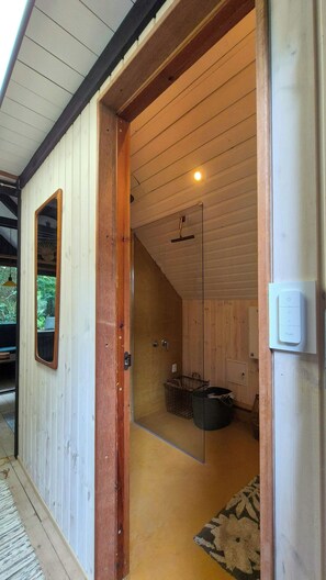 A wooden interior with a glass door leading to a bathroom, a hanging light fixture, and a visible power outlet.