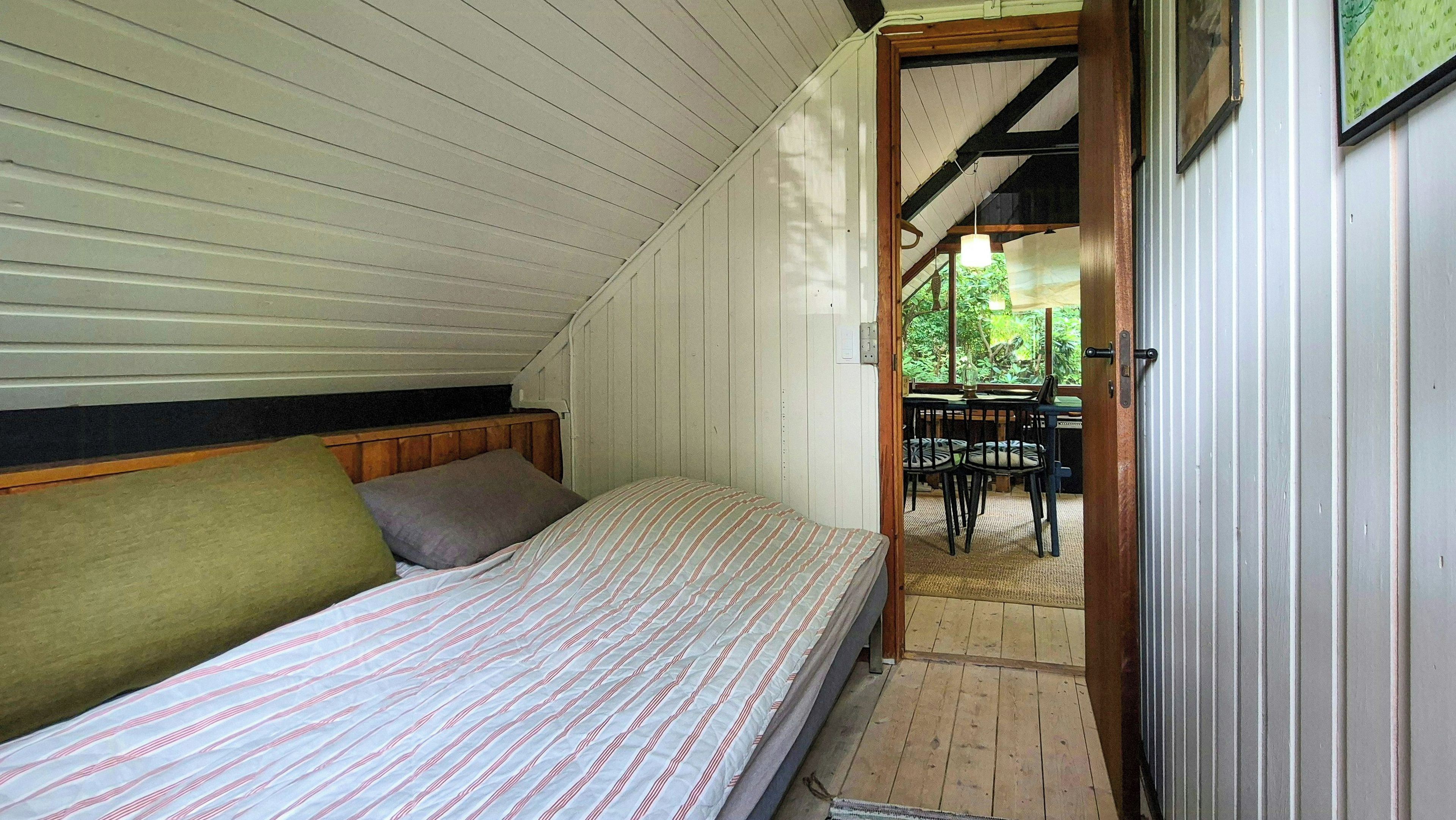 Ein kleines Zimmer mit einem Einzelbett, einem Holzkopfstück und einem Fenster mit Blick auf einen Garten.