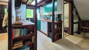 Een compacte keuken met een vaatwasser, een eethoek met een tafel en stoelen, en een boekenplank vol boeken.